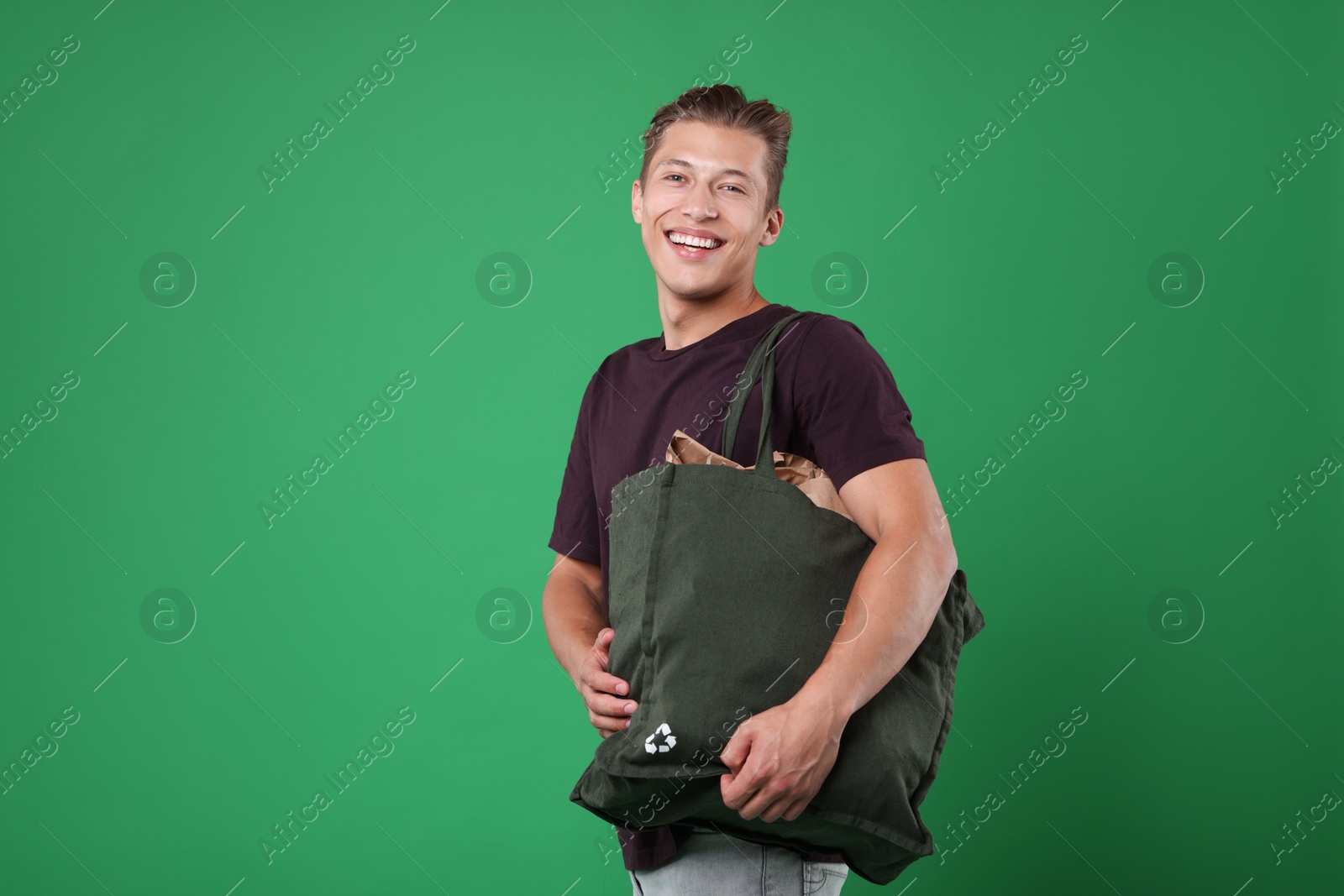 Photo of Recycling. Smiling man with bag full of different waste paper on green background