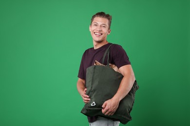 Photo of Recycling. Smiling man with bag full of different waste paper on green background
