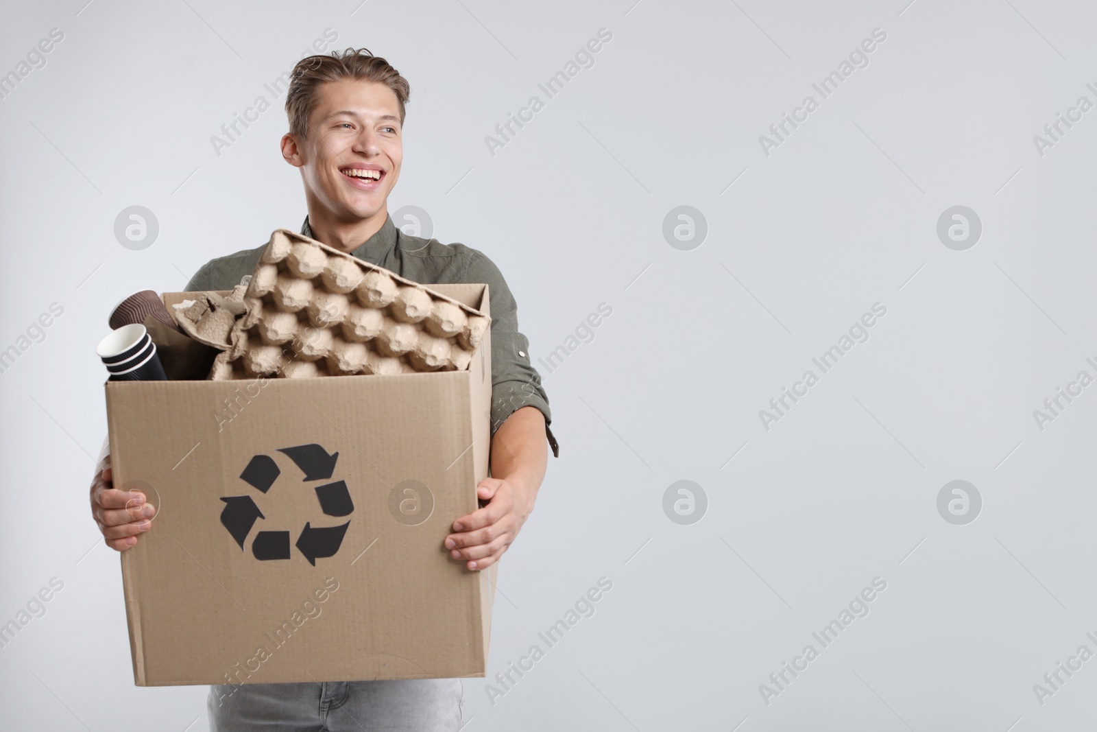 Photo of Recycling. Smiling man holding cardboard box with different waste paper on light background. Space for text