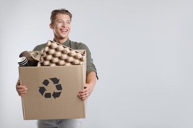 Photo of Recycling. Smiling man holding cardboard box with different waste paper on light background. Space for text