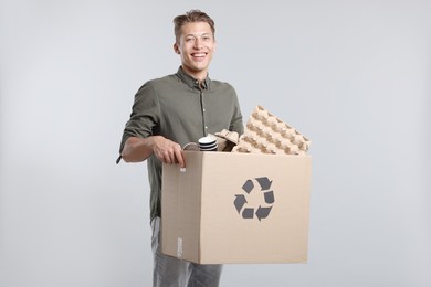 Photo of Recycling. Smiling man holding cardboard box with different waste paper on light background