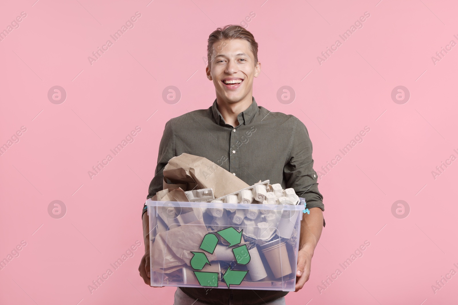 Recycling. Smiling man holding plastic box with different waste paper on pink background Photo of Recycling. Smiling man holding plastic box with different waste paper on pink background