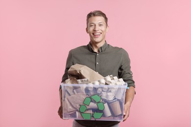Photo of Recycling. Smiling man holding plastic box with different waste paper on pink background