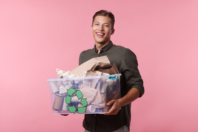 Photo of Recycling. Smiling man holding plastic box with different waste paper on pink background