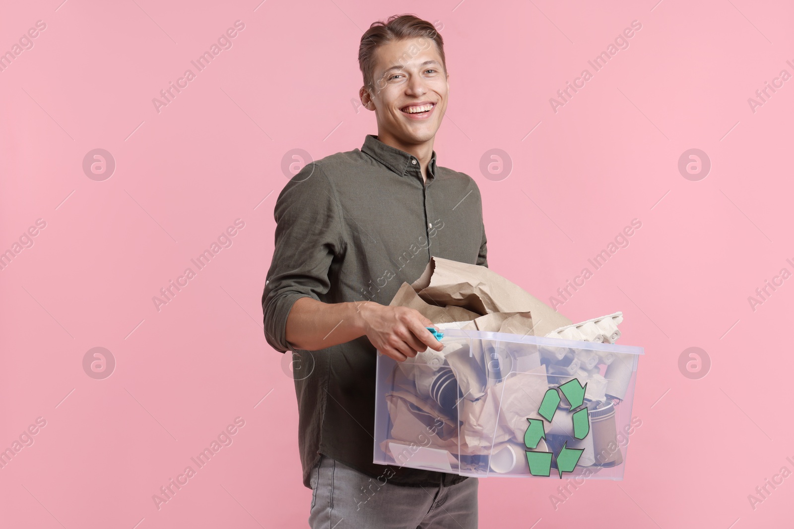 Recycling. Smiling man holding plastic box with different waste paper on pink background Photo of Recycling. Smiling man holding plastic box with different waste paper on pink background