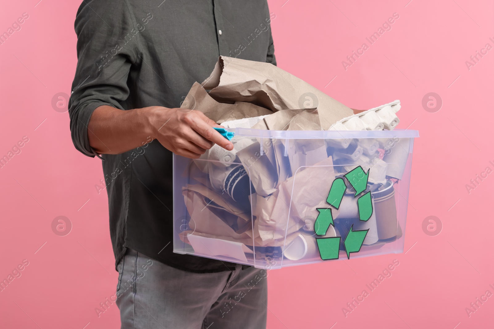 Photo of Recycling. Man holding plastic box with different waste paper on pink background, closeup