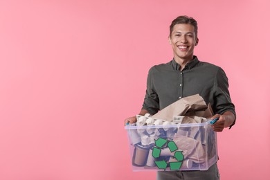 Photo of Recycling. Smiling man holding plastic box with different waste paper on pink background. Space for text