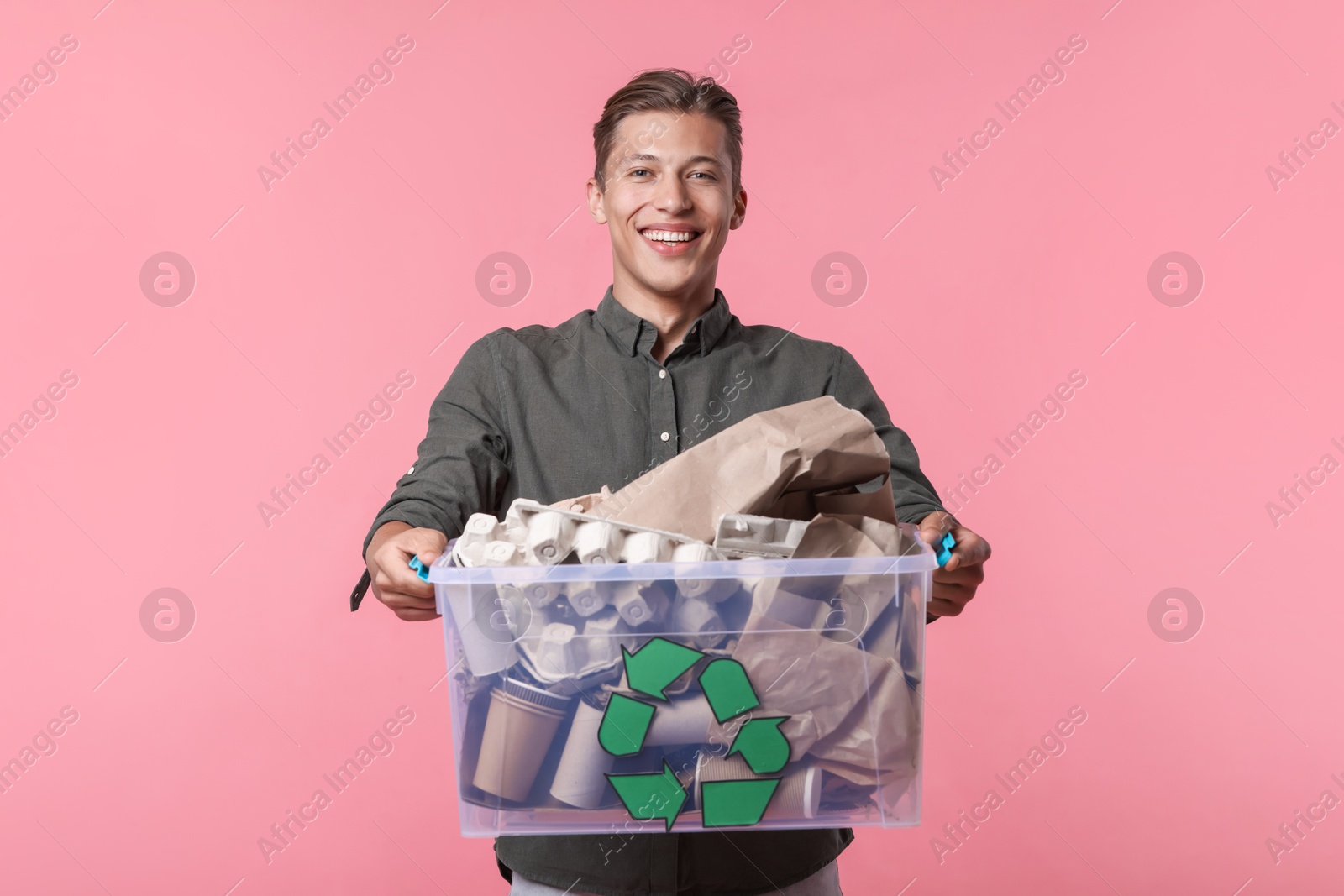 Recycling. Smiling man holding plastic box with different waste paper on pink background Photo of Recycling. Smiling man holding plastic box with different waste paper on pink background
