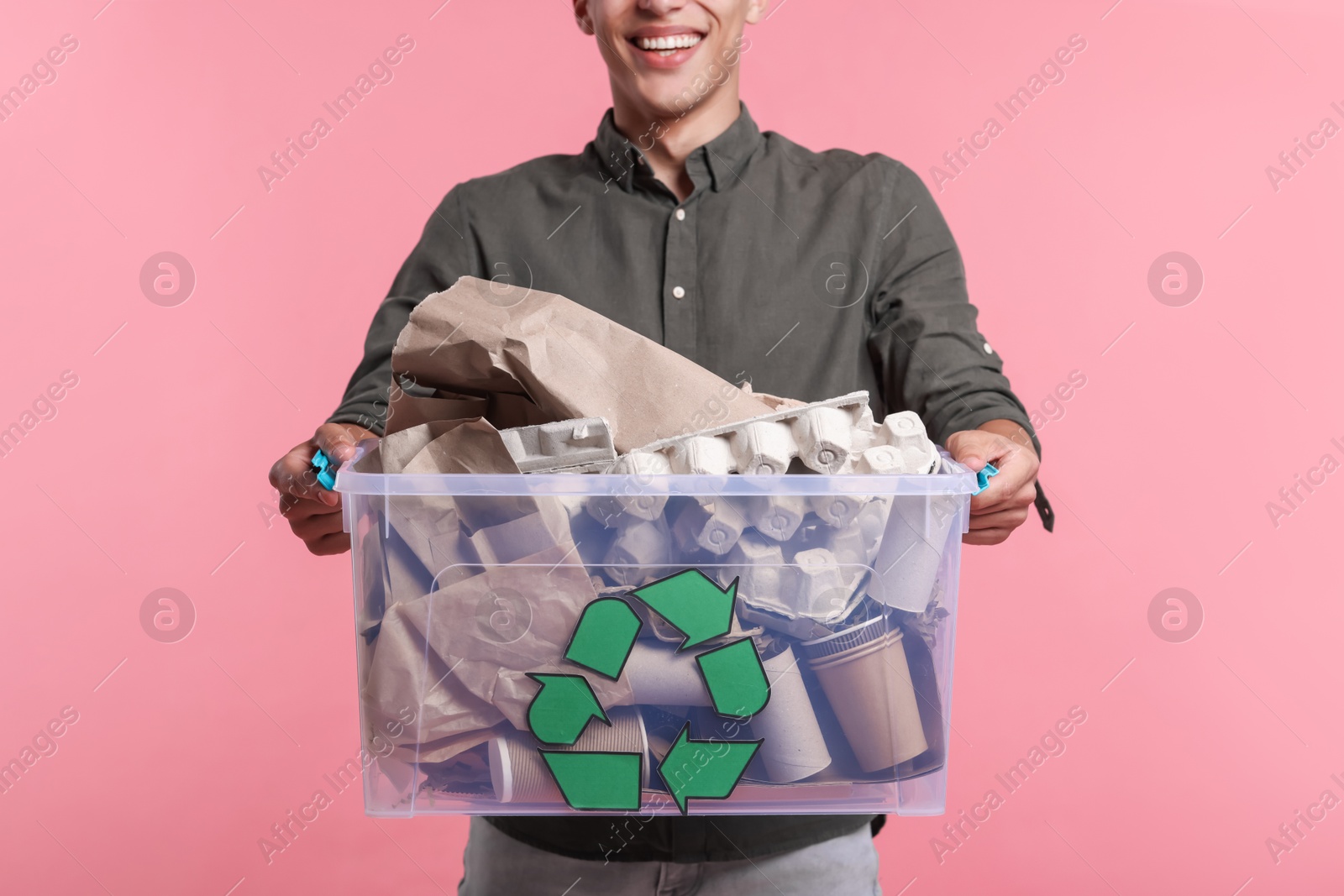 Photo of Recycling. Man holding plastic box with different waste paper on pink background, closeup