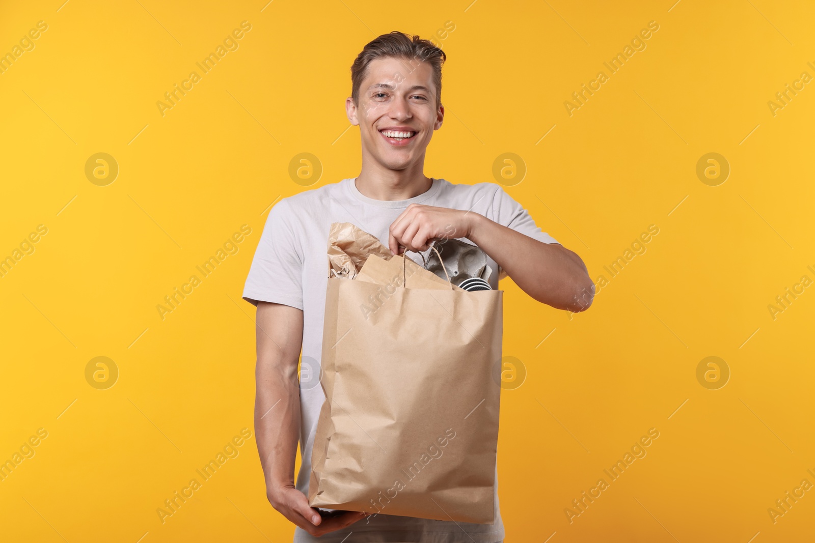 Recycling. Smiling man with bag full of different waste paper on yellow background Photo of Recycling. Smiling man with bag full of different waste paper on yellow background
