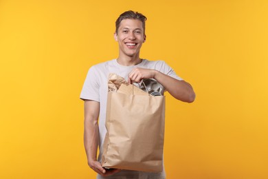 Photo of Recycling. Smiling man with bag full of different waste paper on yellow background