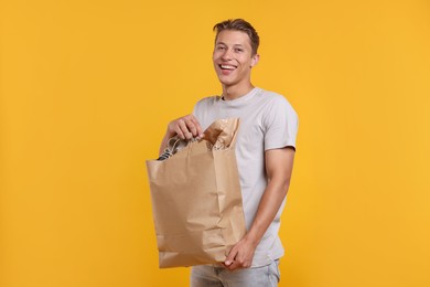 Photo of Recycling. Smiling man with bag full of different waste paper on yellow background
