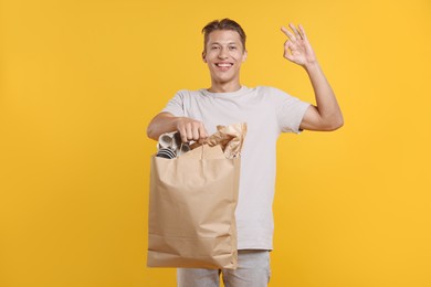 Photo of Recycling. Smiling man with bag full of different waste paper showing OK gesture on yellow background