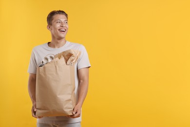 Photo of Recycling. Smiling man with bag full of different waste paper on yellow background. Space for text