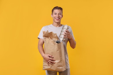 Photo of Recycling. Smiling man with bag full of different waste paper on yellow background
