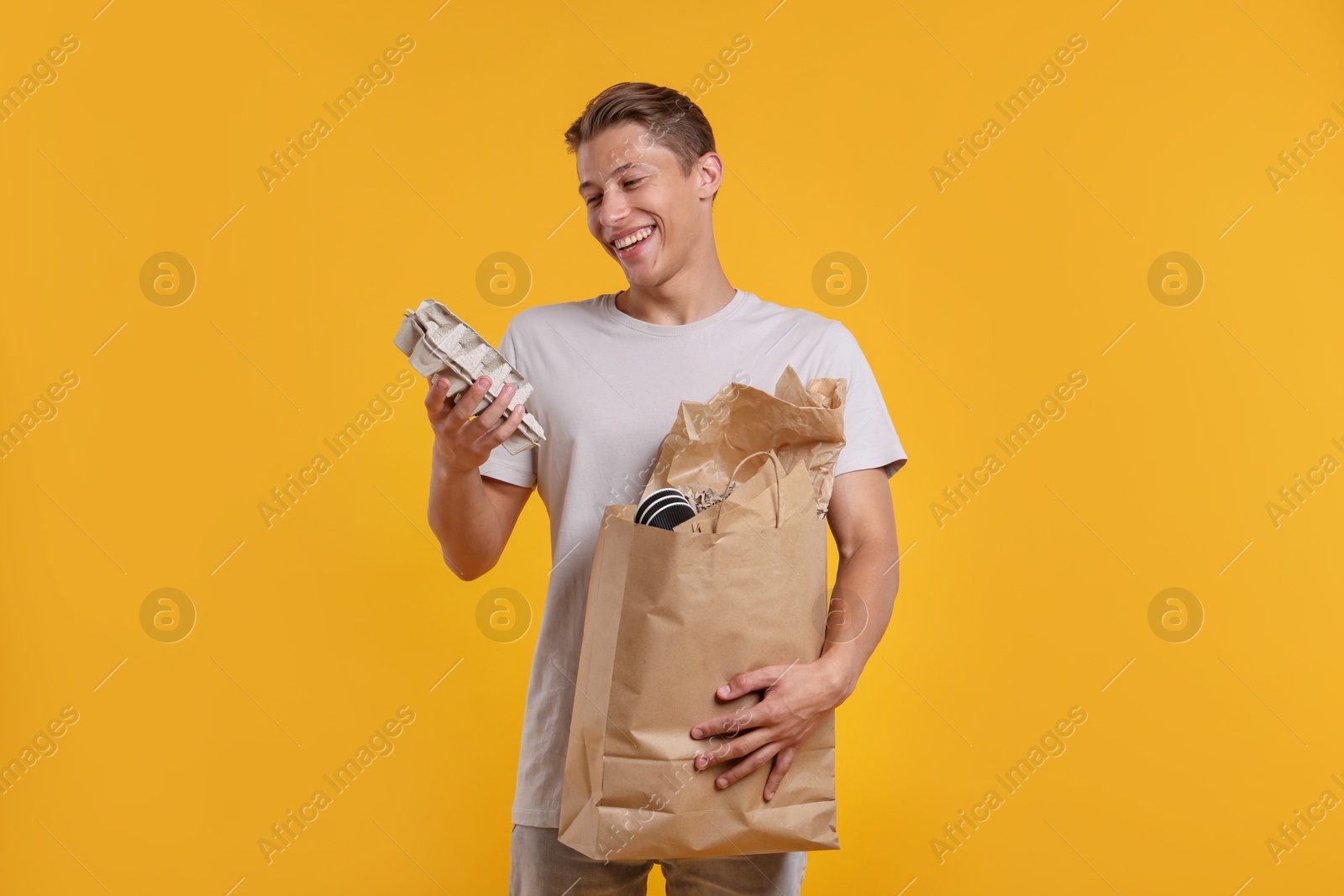 Recycling. Smiling man with bag full of different waste paper on yellow background Photo of Recycling. Smiling man with bag full of different waste paper on yellow background