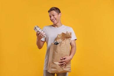 Photo of Recycling. Smiling man with bag full of different waste paper on yellow background