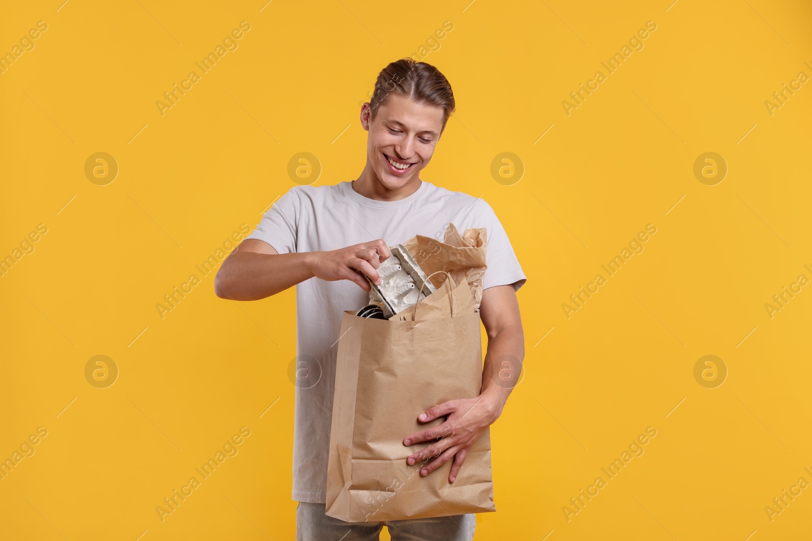 Recycling. Smiling man with bag full of different waste paper on yellow background Photo of Recycling. Smiling man with bag full of different waste paper on yellow background