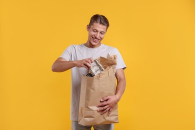 Photo of Recycling. Smiling man with bag full of different waste paper on yellow background
