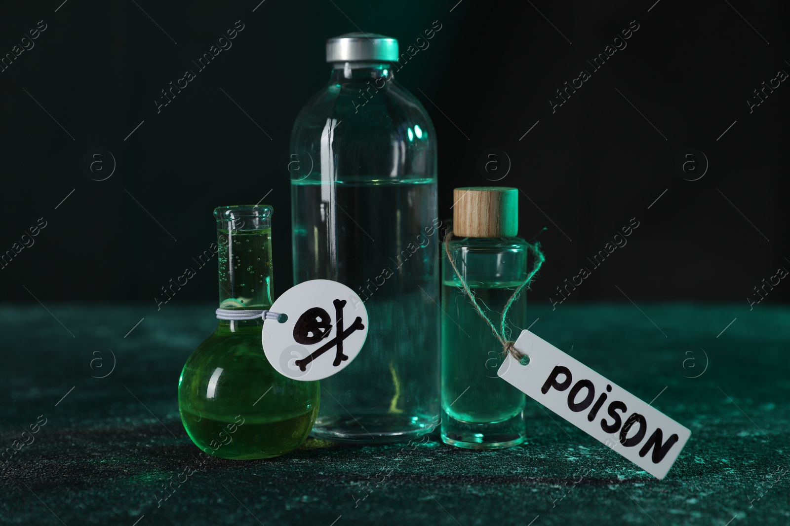 Photo of Bottles of poisons with warning sign on textured table against dark background, closeup
