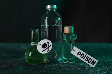 Photo of Bottles of poisons with warning sign on textured table against dark background, closeup