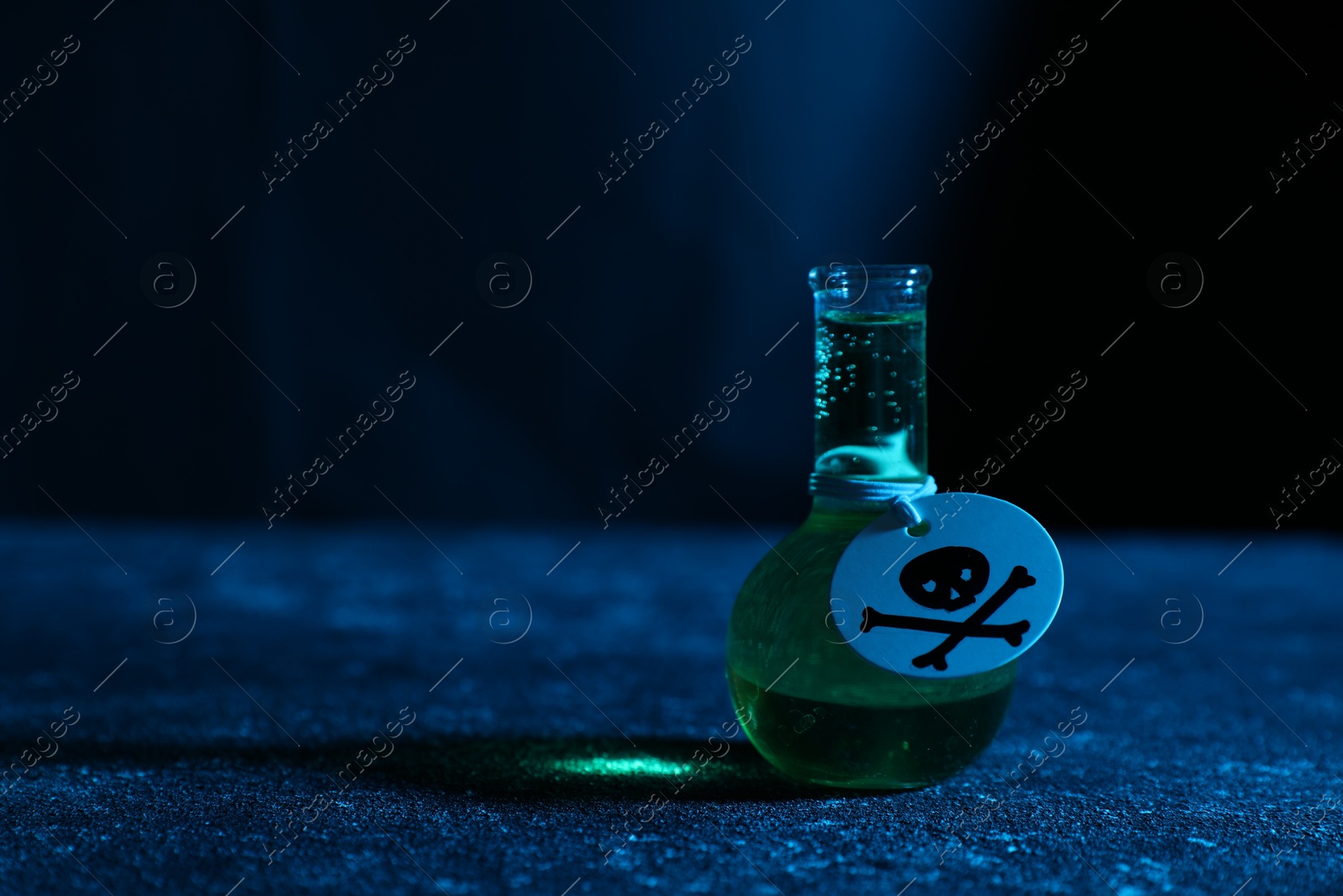 Photo of Flask of poison with warning sign on textured table against dark background, closeup. Space for text