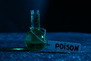 Photo of Flask with poison on textured table against dark background, closeup