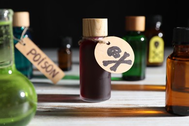 Photo of Bottles of poisons with warning sign on wooden table against black background, closeup