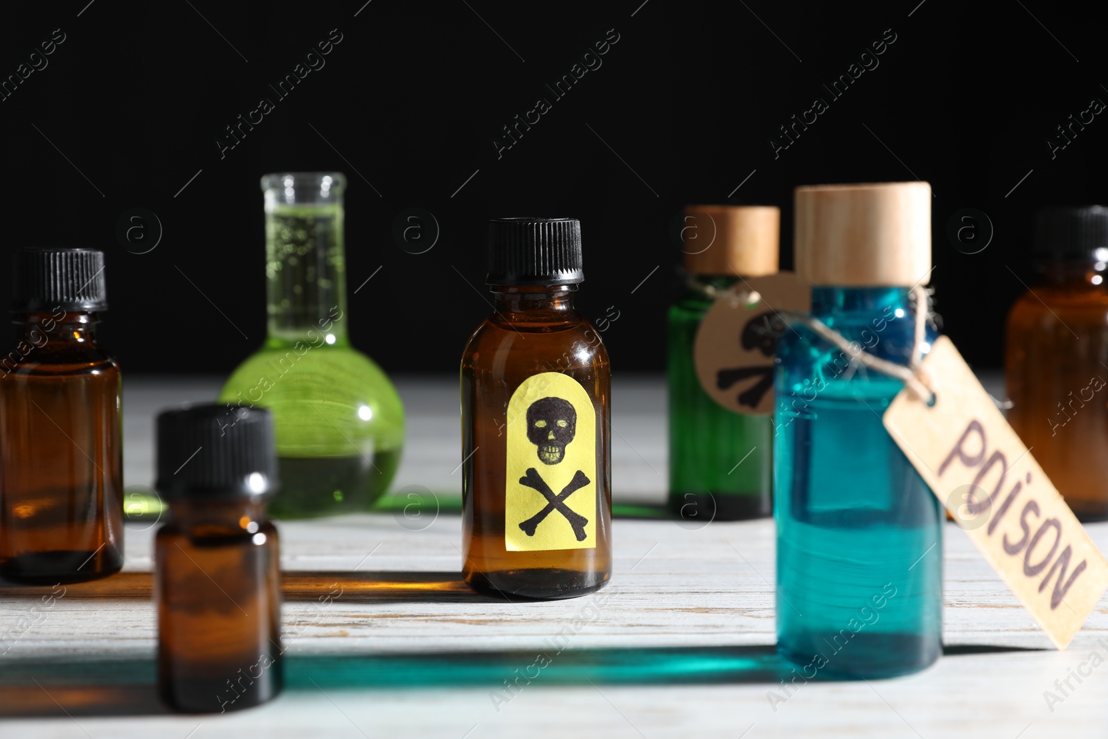 Photo of Bottles of poisons with warning sign on wooden table against black background, closeup