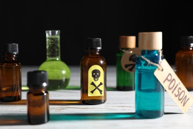 Photo of Bottles of poisons with warning sign on wooden table against black background, closeup
