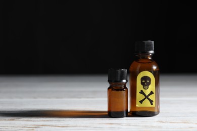 Photo of Bottles of poisons with warning sign on wooden table against black background, space for text