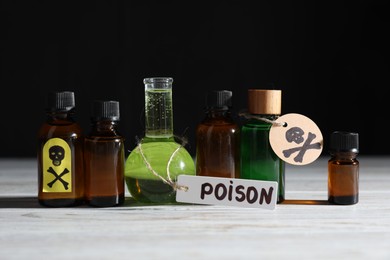 Photo of Bottles of poisons with warning sign on wooden table against black background