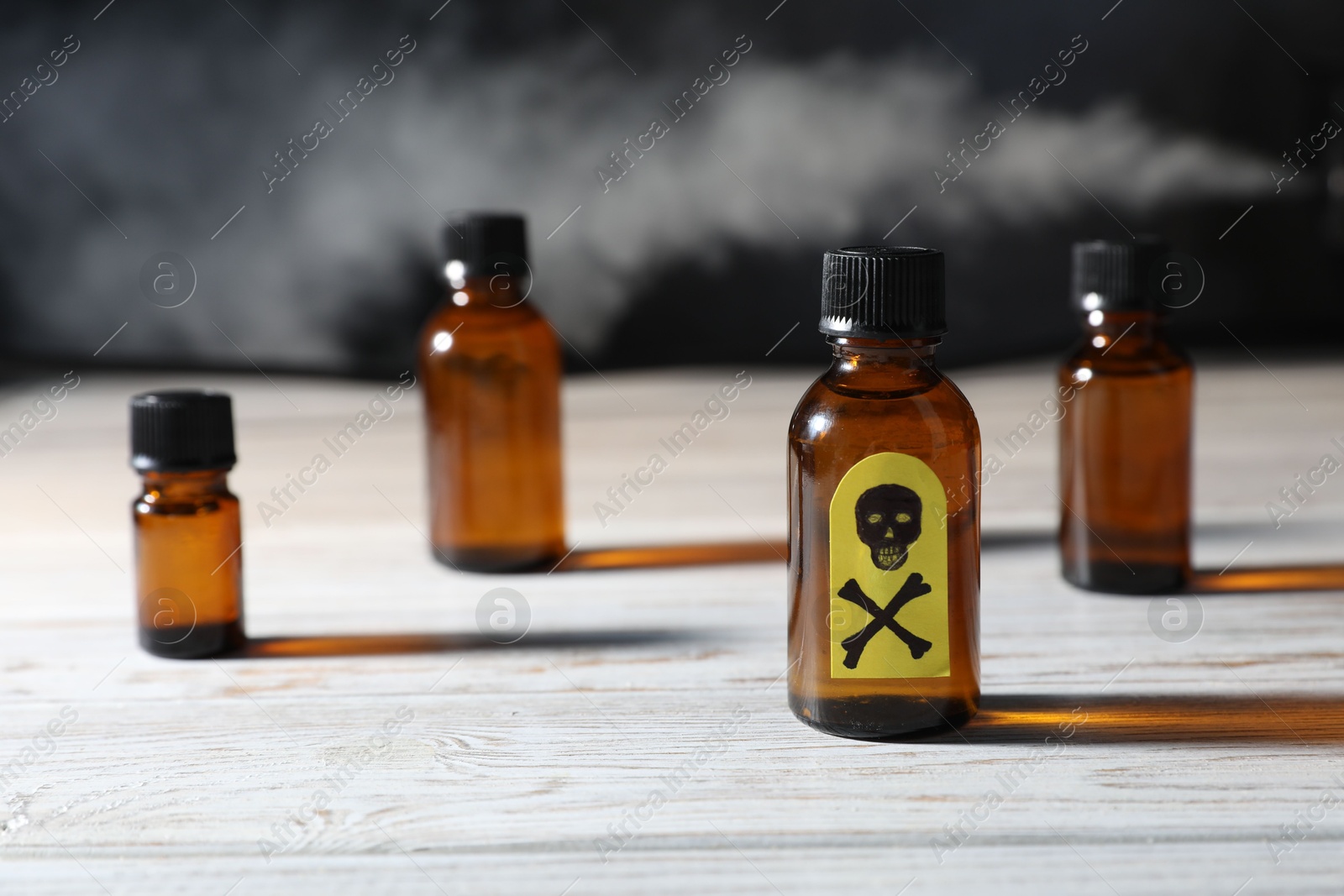 Photo of Bottles of poisons with warning sign on wooden table against dark background with smoke, closeup