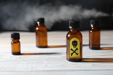Photo of Bottles of poisons with warning sign on wooden table against dark background with smoke, closeup