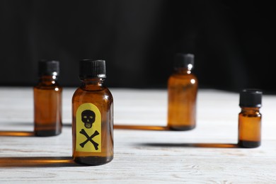 Photo of Bottles of poisons with warning sign on wooden table against dark background, closeup