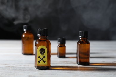 Photo of Bottles of poisons with warning sign on wooden table against dark background with smoke, closeup