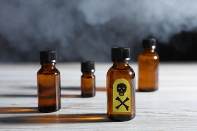 Photo of Bottles of poisons with warning sign on wooden table against dark background with smoke, closeup