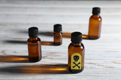 Photo of Bottles of poisons with warning sign on wooden table, closeup