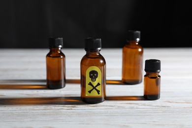 Photo of Bottles of poisons with warning sign on wooden table against dark background, closeup