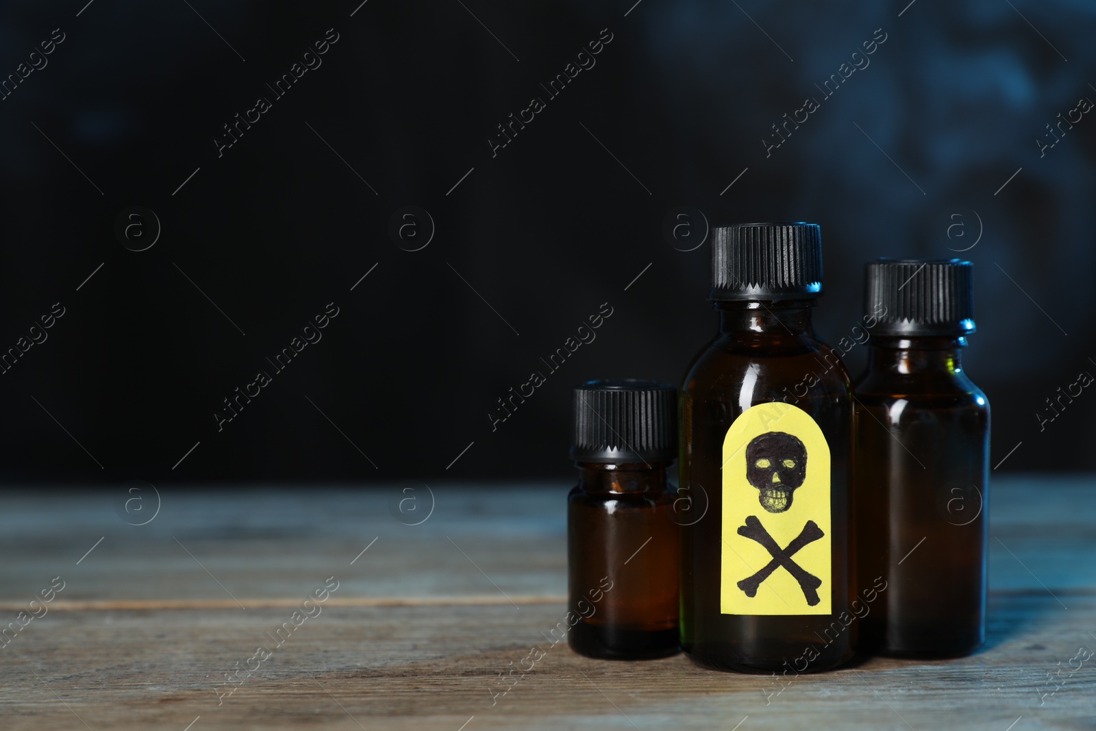 Photo of Bottles of poisons with warning sign on wooden table against dark background with smoke, space for text