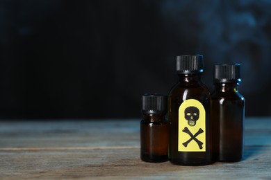 Photo of Bottles of poisons with warning sign on wooden table against dark background with smoke, space for text