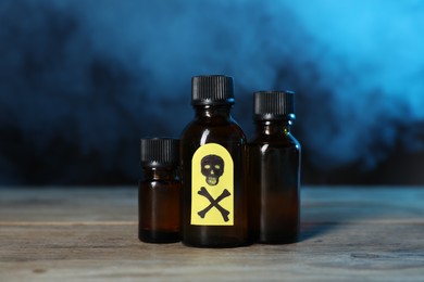 Photo of Bottles of poisons with warning sign on wooden table against dark background with smoke