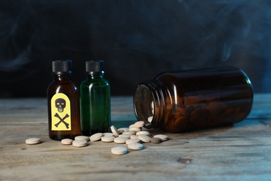 Photo of Bottles of poisons with warning sign on wooden table against dark background with smoke, closeup