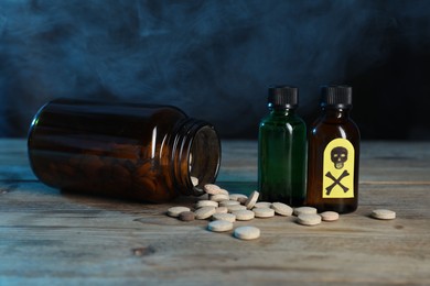 Photo of Bottles of poisons with warning sign on wooden table against dark background with smoke, closeup