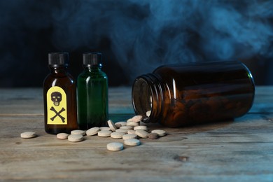 Photo of Bottles of poisons with warning sign on wooden table against dark background with smoke, closeup