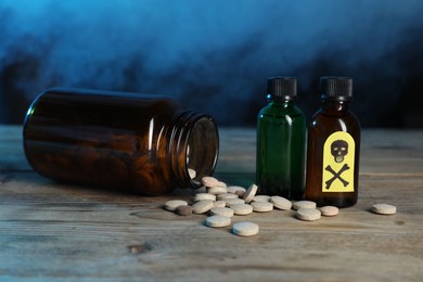 Photo of Bottles of poisons with warning sign on wooden table against dark background with smoke, closeup