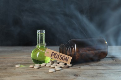 Photo of Bottles of poisons on wooden table against dark background with smoke, closeup