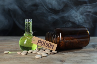 Photo of Bottles of poisons on wooden table against dark background with smoke, closeup