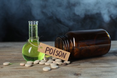 Photo of Bottles of poisons on wooden table against dark background with smoke, closeup