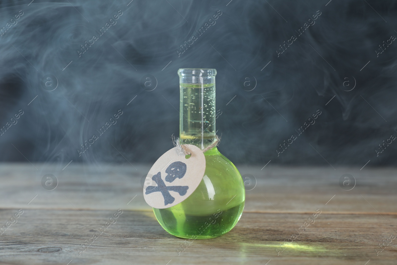 Photo of Flask of poison with warning sign on wooden table against dark background with smoke
